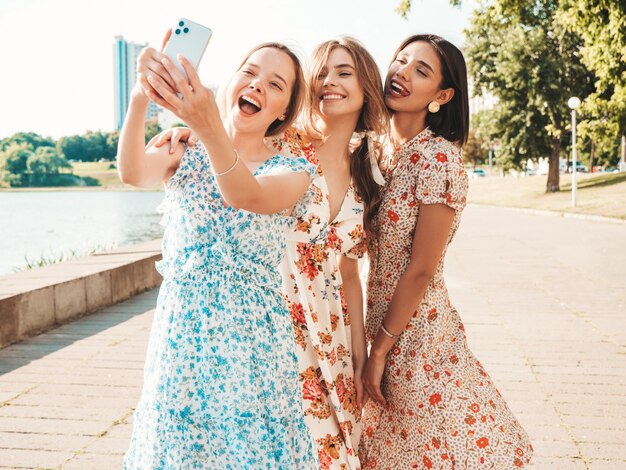 Trois belles filles souriantes en robe d'été à la mode prenant selfie