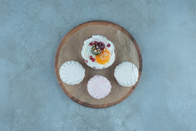 Trois biscuits et un gâteau sur une planche de bois sur du marbre.