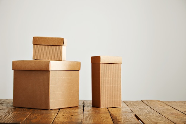 Trois boîtes en carton beige de tailles différentes disposées au-dessus d'une table rustique marron dans un studio aux murs blancs