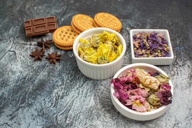 Trois bols de fleurs sèches avec du chocolat et des biscuits sur fond gris