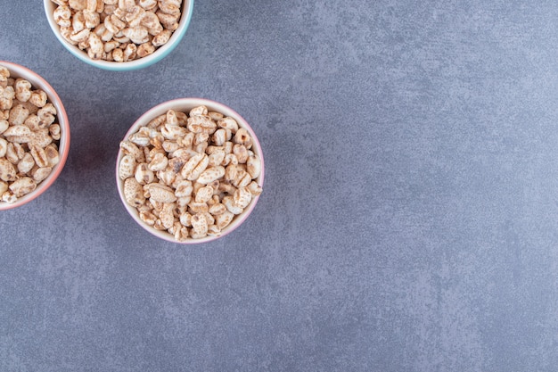 Trois bols de muesli sucré, sur la table en marbre.