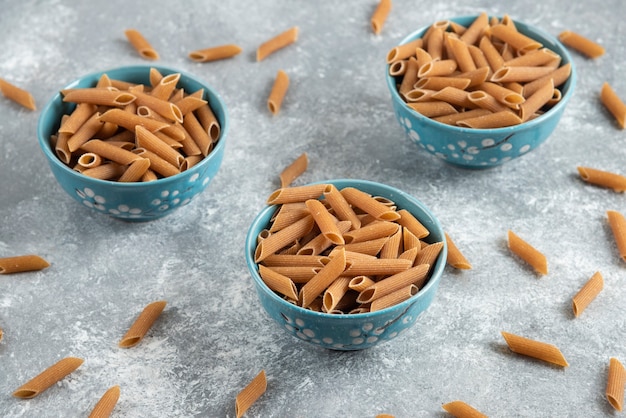 Photo gratuite trois bols remplis de pâtes crues brunes sur une surface grise.