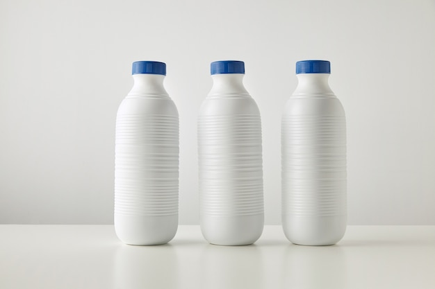 Trois bouteilles en plastique blanc à rayures blanches avec des bouchons bleus en ligne isolé sur table au centre