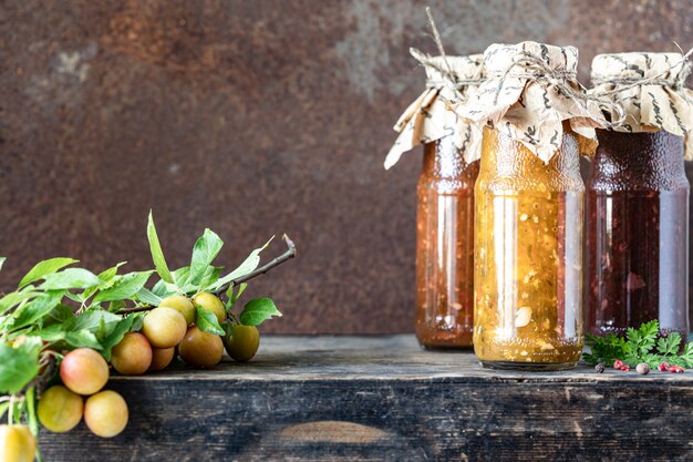 Trois bouteilles en verre d'un assortiment de sauce tkemali géorgienne avec des ingrédients sur une table en bois rustique