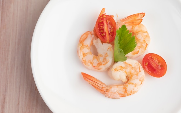 Photo gratuite trois crevettes fraîches et demi-tomates dans une assiette blanche sur un bois.