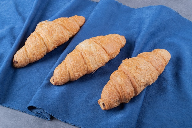 Trois croissants français frais sur une serviette bleue.