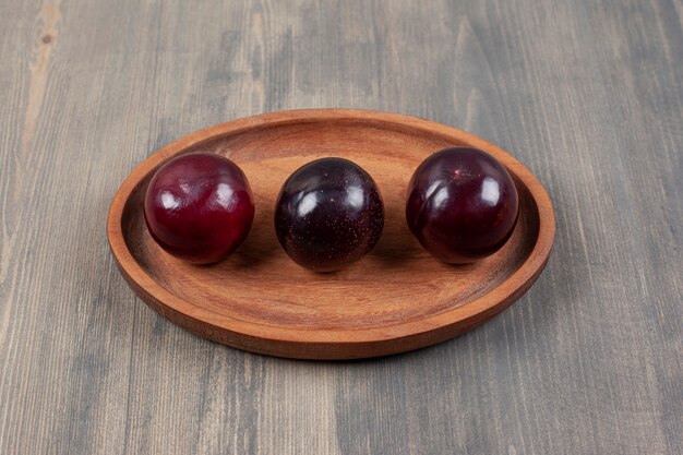 Trois délicieuses prunes sur une assiette en bois. Photo de haute qualité