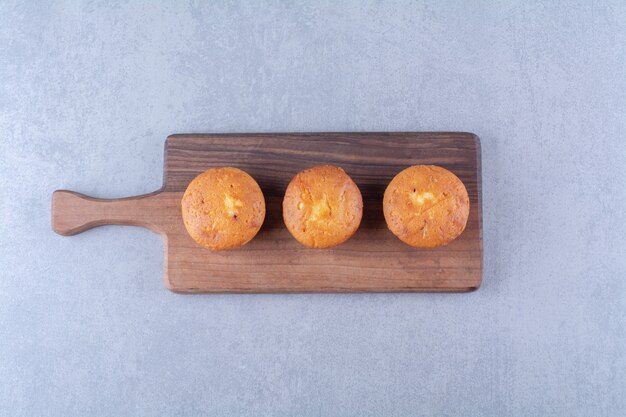 Trois délicieux cupcakes sucrés sur une planche à découper en bois.