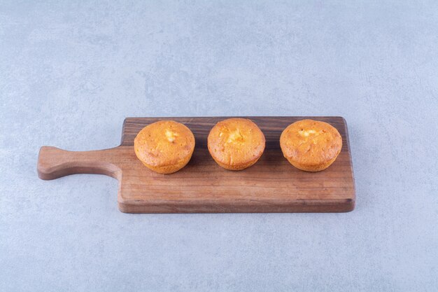 Trois délicieux cupcakes sucrés sur une planche à découper en bois