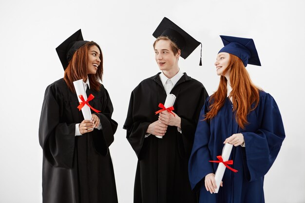 Trois diplômés heureux souriant parlant détenant des diplômes.