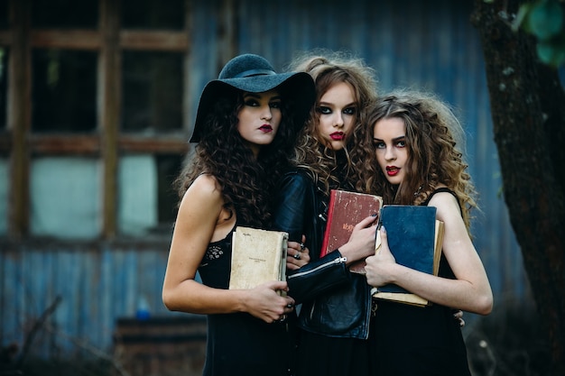 Photo gratuite trois femmes d'époque en tant que sorcières, posent devant un bâtiment abandonné avec des livres à la main à la veille d'halloween