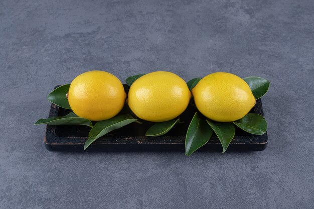 Trois feuilles de citron et de citron frais sur planche de bois noire.