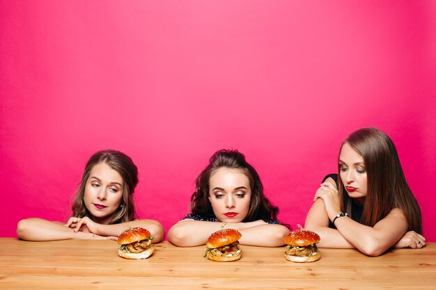 Trois filles tristes au régime regardant des hamburgers sur la table