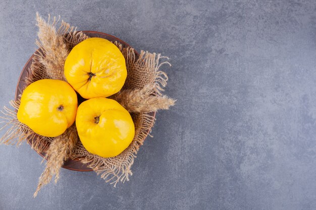 Trois fruits de coing frais avec des épis de blé placés sur une table en pierre.