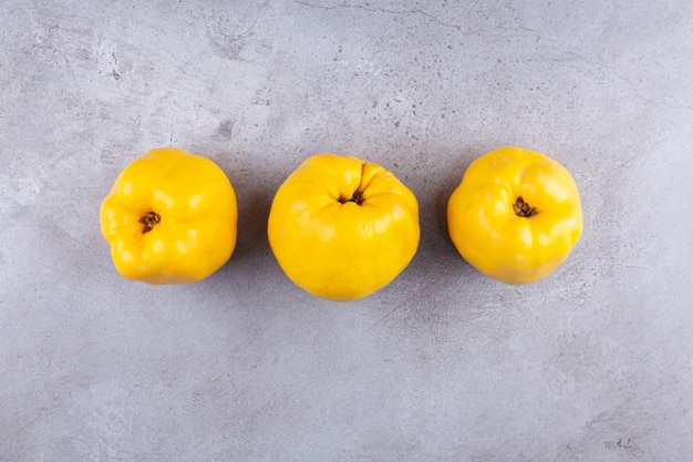 Trois fruits de coing jaune mûr sur fond de pierre.