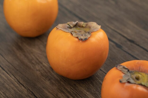 Trois fruits de kaki mûrs placés sur une surface en bois