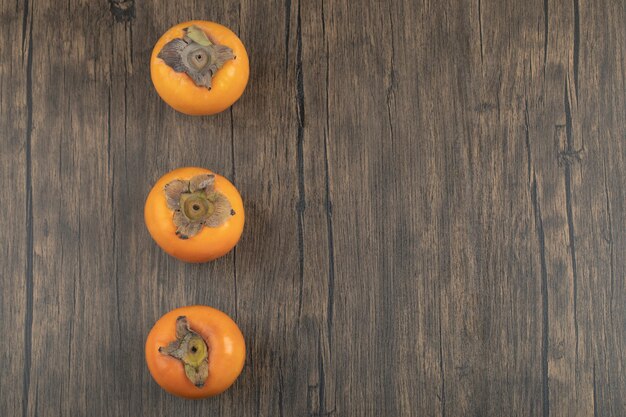 Trois fruits kakis mûrs placés sur une surface en bois