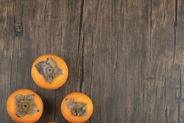 Trois fruits kakis mûrs placés sur une surface en bois