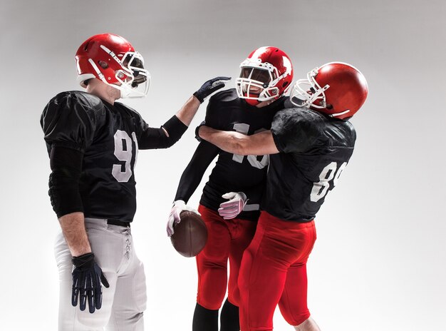 Les trois hommes de fitness caucasiens en tant que joueurs de football américain se faisant passer pour des gagnants sur fond blanc et se réjouissant