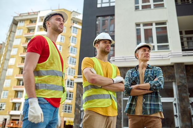 Photo gratuite trois hommes regardant de côté au chantier de construction