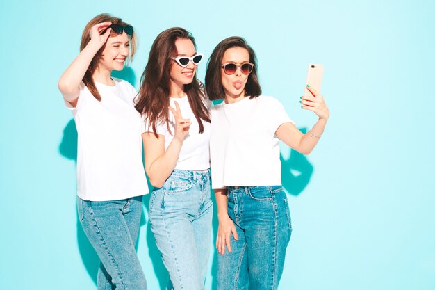 Trois jeunes belles femmes hipster souriantes dans des vêtements en jean et t-shirt blancs à la mode du même été