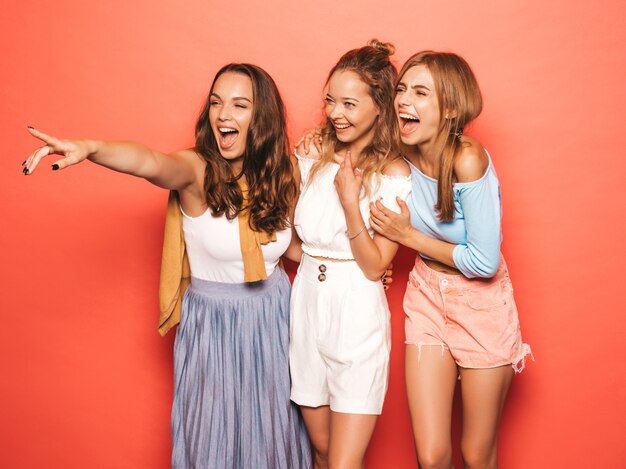 Trois jeunes belles filles hipster souriantes dans des vêtements d'été à la mode. Femmes insouciantes sexy posant près du mur rose. Des modèles positifs qui s'amusent.