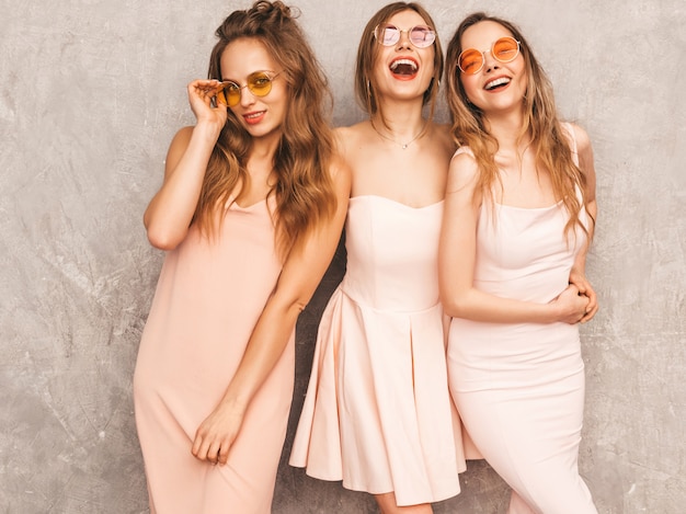 Trois jeunes belles filles souriantes dans des robes rose pâle d'été à la mode. Femmes insouciantes sexy posant. Modèles positifs en lunettes de soleil rondes s'amusant