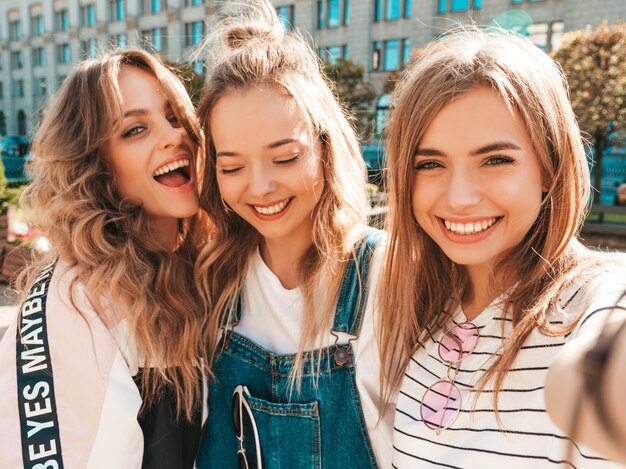 Trois jeunes femmes souriantes hipster dans des vêtements d'été.Filles prenant des photos d'autoportrait selfie sur smartphone.Modèles posant dans la rue.Femme montrant des émotions positives