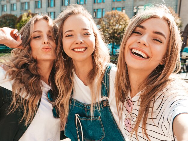 Trois jeunes femmes souriantes hipster dans des vêtements d'été.Filles prenant des photos d'autoportrait selfie sur smartphone.Modèles posant dans la rue.Femme montrant des émotions positives