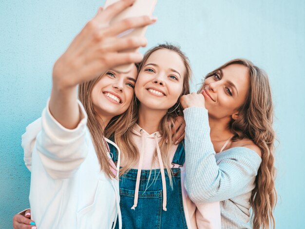 Trois jeunes femmes souriantes hipster en vêtements d'été.Filles prenant des photos d'autoportrait selfie sur smartphone.Modèles posant dans la rue près du mur.Femme montrant des émotions positives