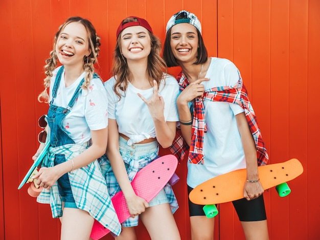 Trois jeunes filles belles souriantes avec des planches à roulettes penny colorées.