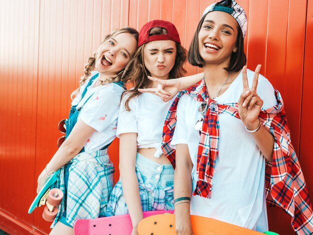 Trois jeunes filles belles souriantes avec des planches à roulettes penny colorées.