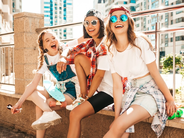 Trois jeunes filles belles souriantes avec des planches à roulettes penny colorées.