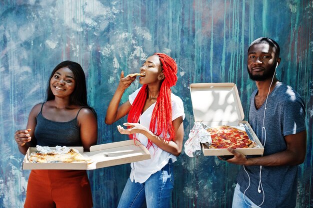 Trois joyeux amis afro-américains tenant des boîtes à pizza contre un mur de peinture