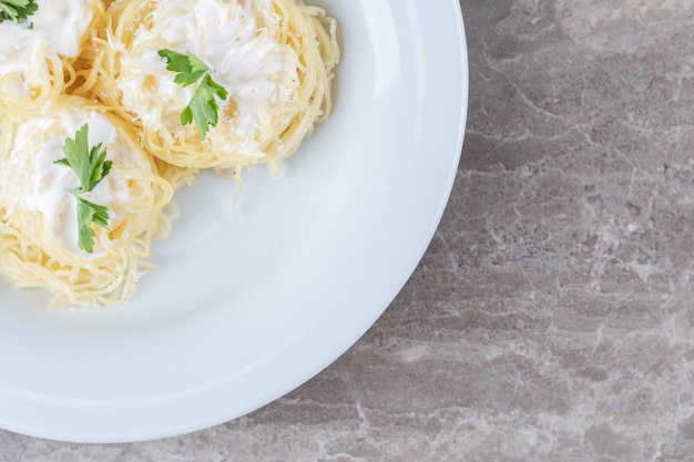 Trois morceaux de spaghetti, yaourt et légumes verts sur l'assiette, sur la surface en marbre.