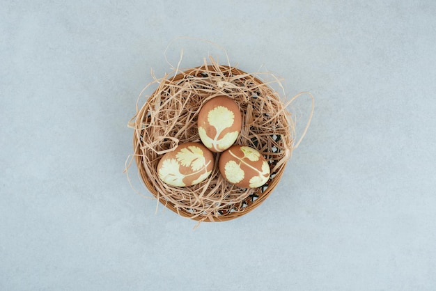 Trois œufs de poule peints dans du foin sur un panier en osier.