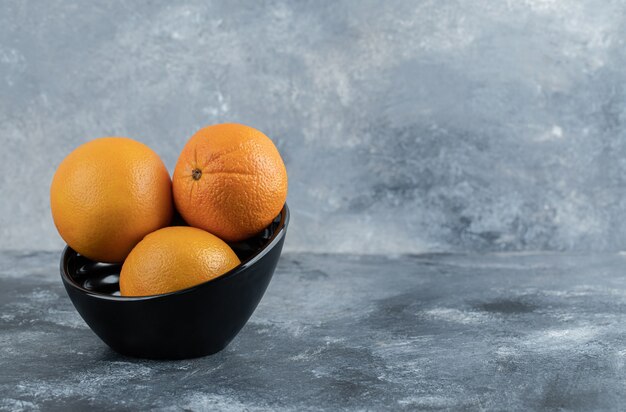 Trois oranges fraîches dans un bol noir.