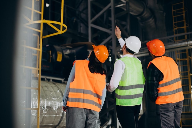 Trois ouvriers d'usine portant des casques de sécurité discutant du plan de fabrication