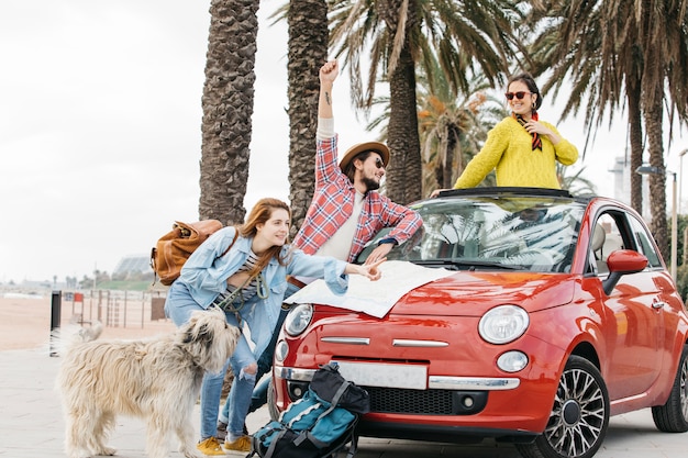 Trois personnes et chien debout près de voiture avec carte routière