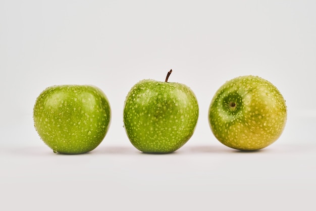 Trois pommes entières sur une surface blanche.