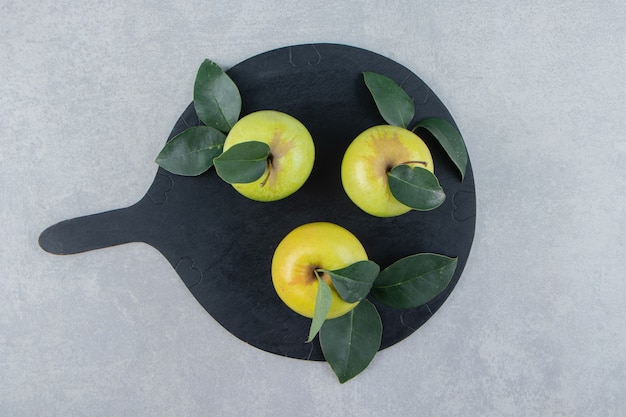 Trois pommes fraîches sur planche de bois noir.