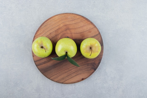 Trois pommes fraîches sur planche de bois.