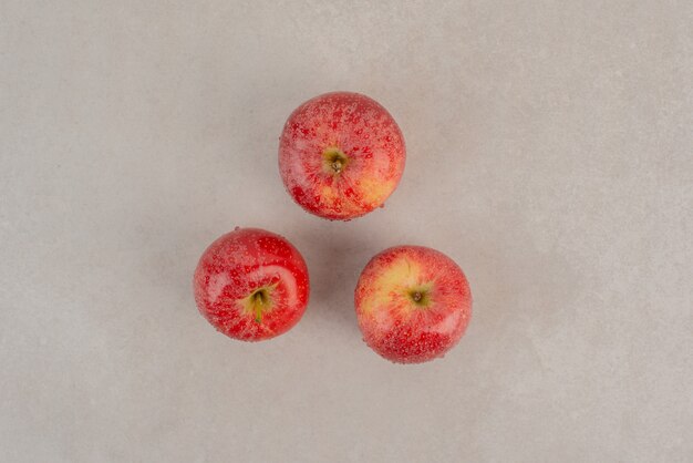 Trois pommes rouges sur une surface en marbre.