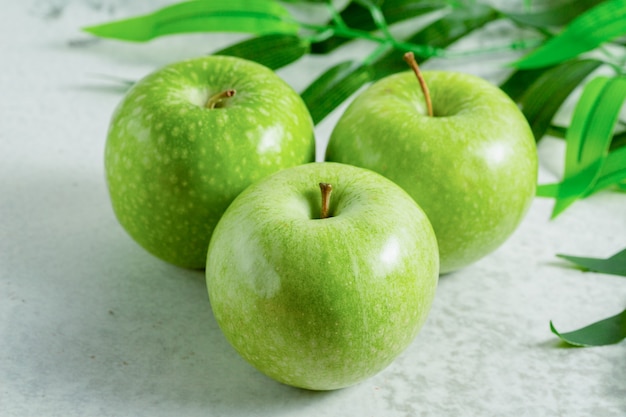 Photo gratuite trois pommes vertes biologiques sur une surface grise.