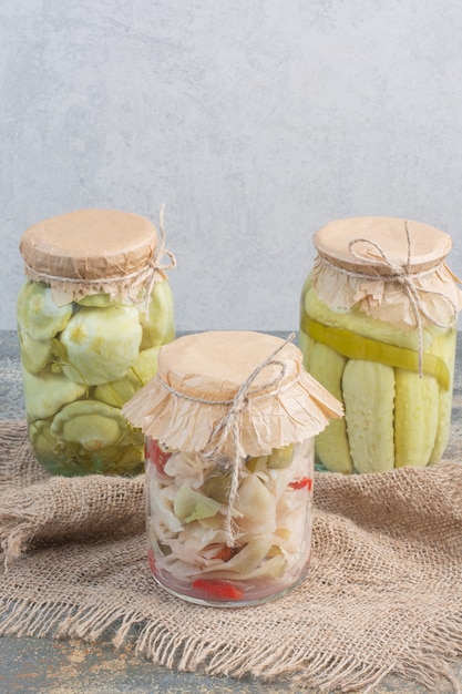 Trois pots pleins de légumes salés sur un sac