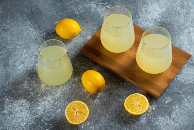 Trois tasses en verre avec du jus de citron frais sur planche de bois.