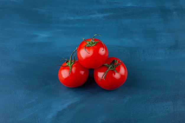 Trois tomates fraîches rouges placées sur une surface bleue.