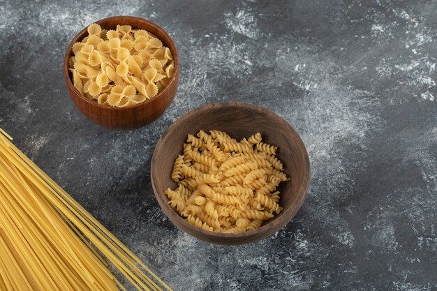 Trois types de pâtes non cuites sur une table en marbre.