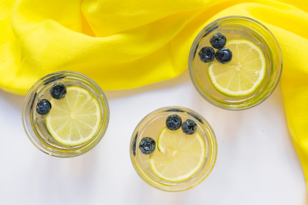 Photo gratuite trois verres de jus de citron avec des bleuets et du tissu jaune