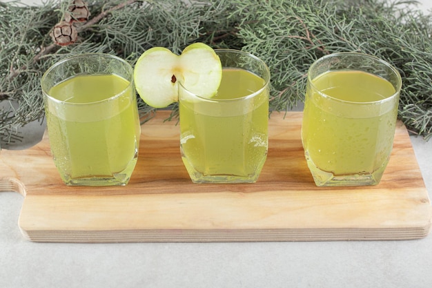 Trois verres de jus avec tranche de pomme sur planche de bois.